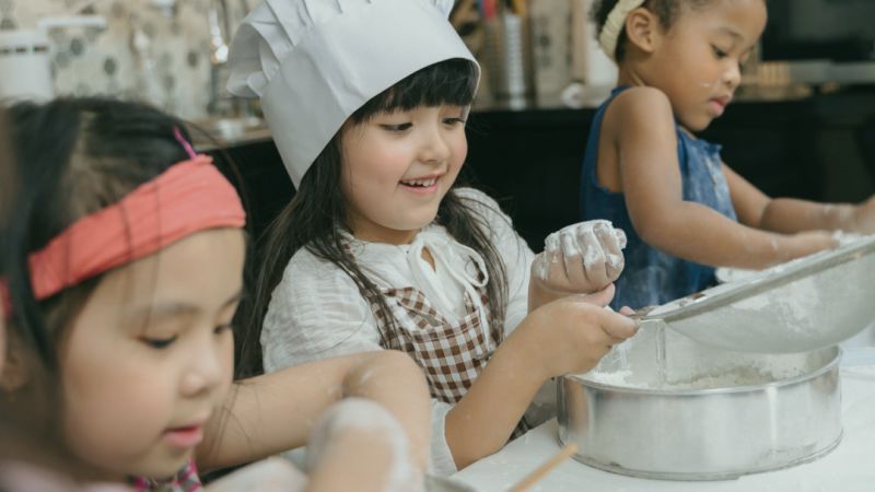 4-H Cooking Club advertisement image. Shows three young girls in the kitchen mixing ingredients. 